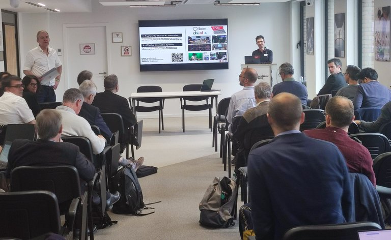 Lecture room of the ERCIM Visionary Event, which took place on 16 April 2024, with Abdallah al Ali of CWI standing as a speaker, and Han La Poutré from CWI, who is ERCIM's Vice President, standing on the left, in front of the audience.