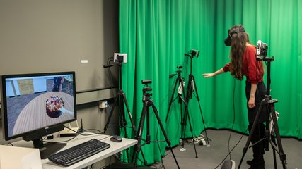 Woman with VR glasses walks around in a virtual environment, shown an a computer screen