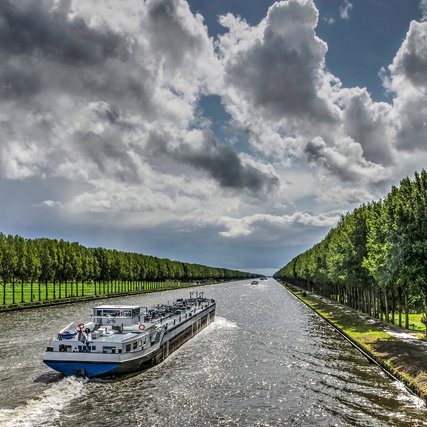 Inland barge on the long straight tree-lined Amsterdam-Rhine canal just south of Amsterdam on a day in summer with dramatic cloud formations