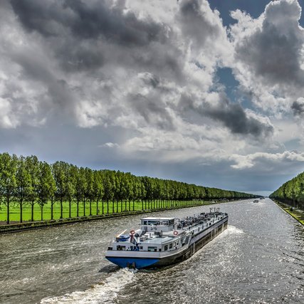 Inland barge on the long straight tree-lined Amsterdam-Rhine canal just south of Amsterdam on a day in summer with dramatic cloud formations