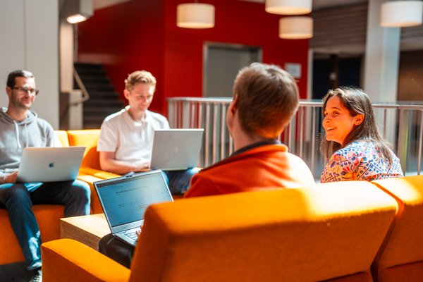 Young researchers sitting on bright coloured seats with their laptops, discussing.