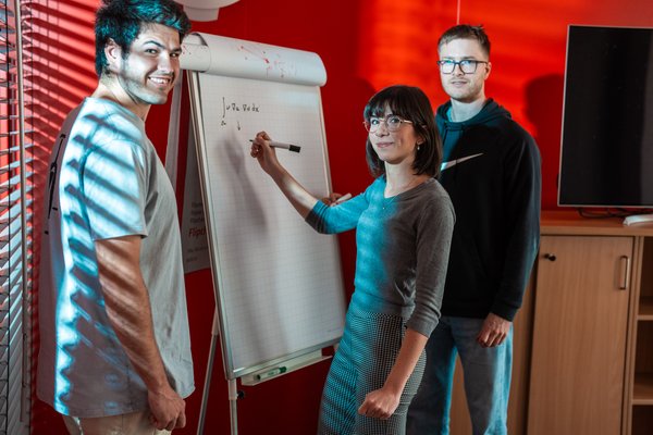 Three students in front of a writing board.