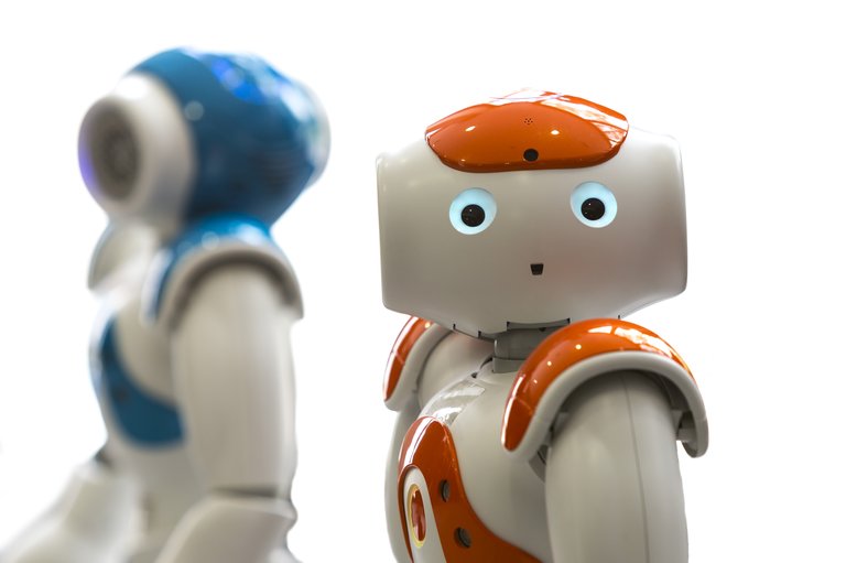 Small robots with human face and body - humanoid. Artificial Intelligence - AI. Orange and blue robots isolated on white background.